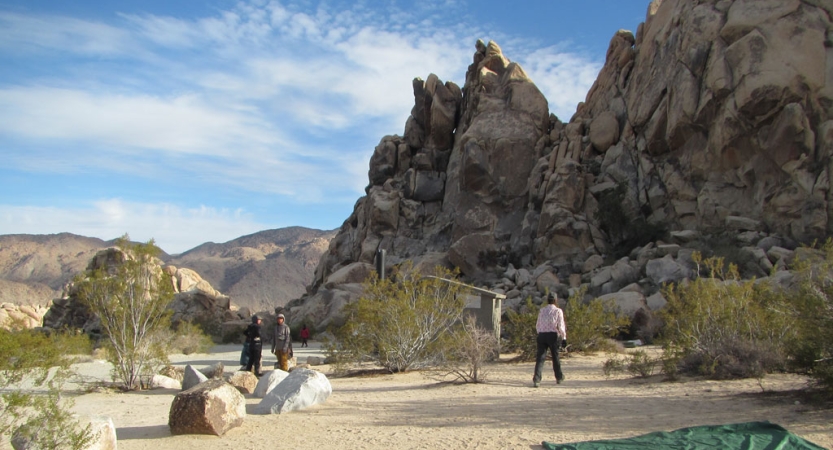 a small group of people set up camp in a desert landscape among tall rock formations and distant mountains